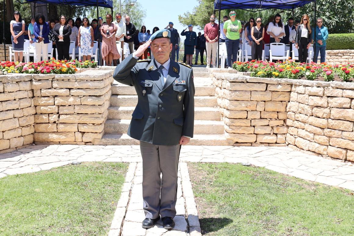 A man in military uniform salutes the camera, with a crowd of people behind him